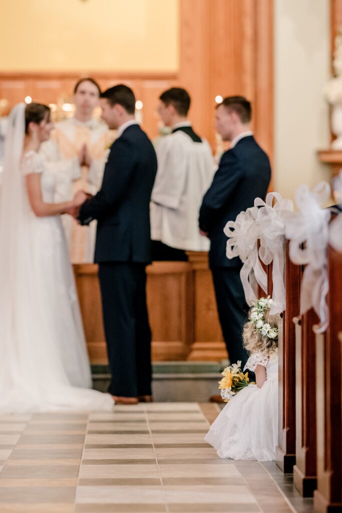 A flower girl peeking out of the pew during the wedding vows