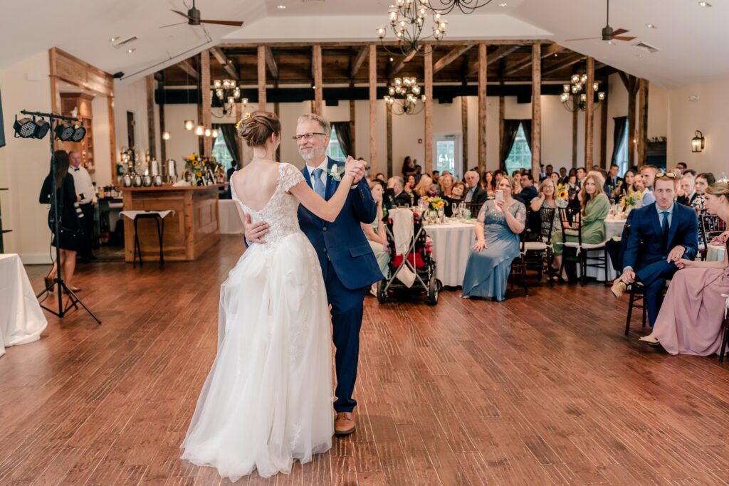 A bride dancing with her father as guests watch from their tables