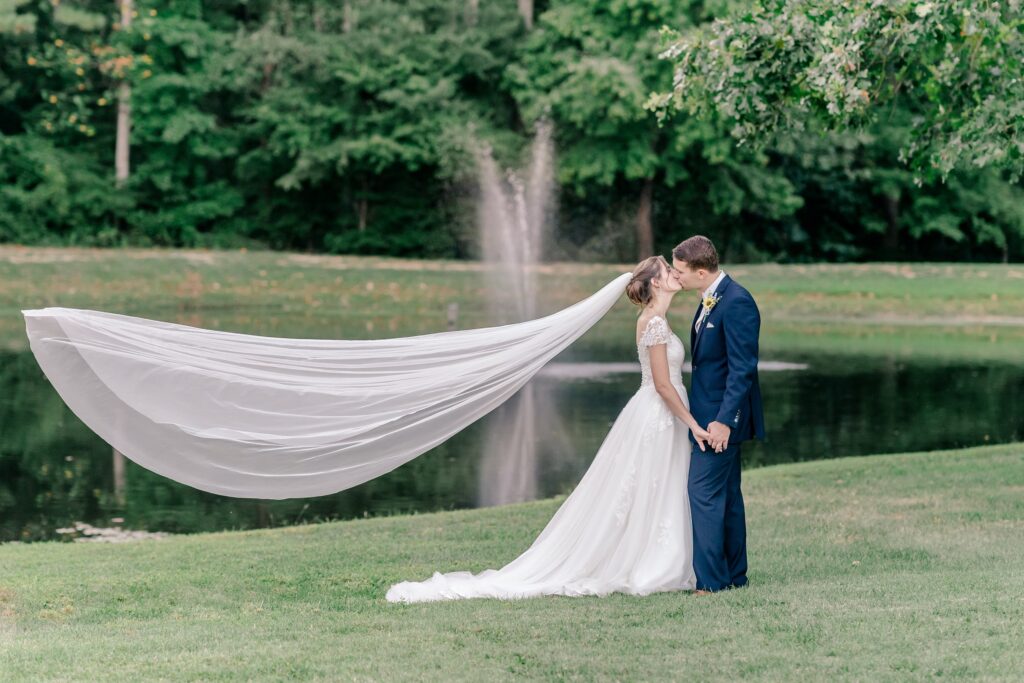 A bride and groom share a kiss as her veil flies behind her during their Catholic wedding in Fredericksburg, VA