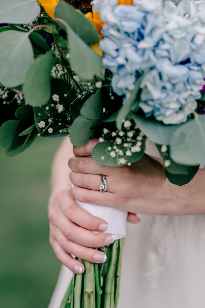 A close up of a bride's hands holding her bouquet with her wedding ring set in focus