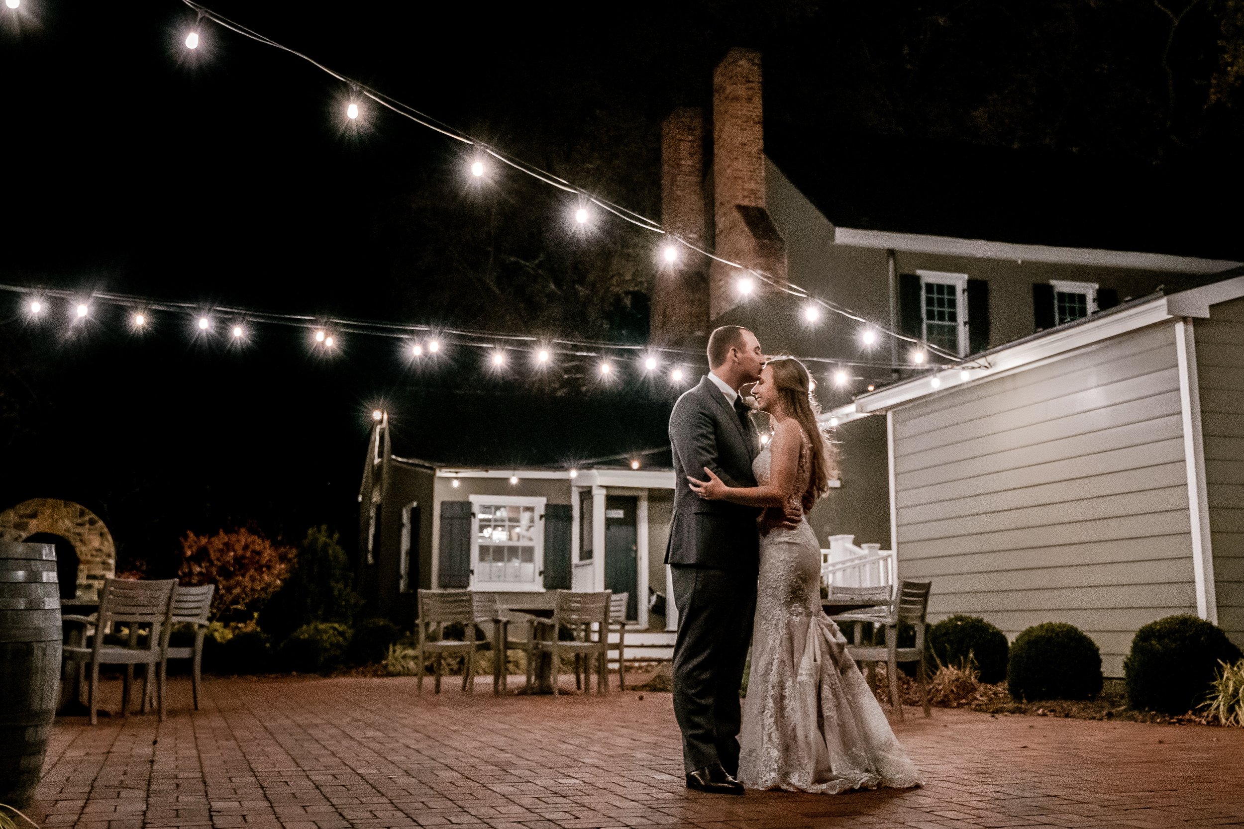 A bride and groom pose for a night portrait under string lights during their wedding at Fleetwood Farm Winery in Leesburg Virginia