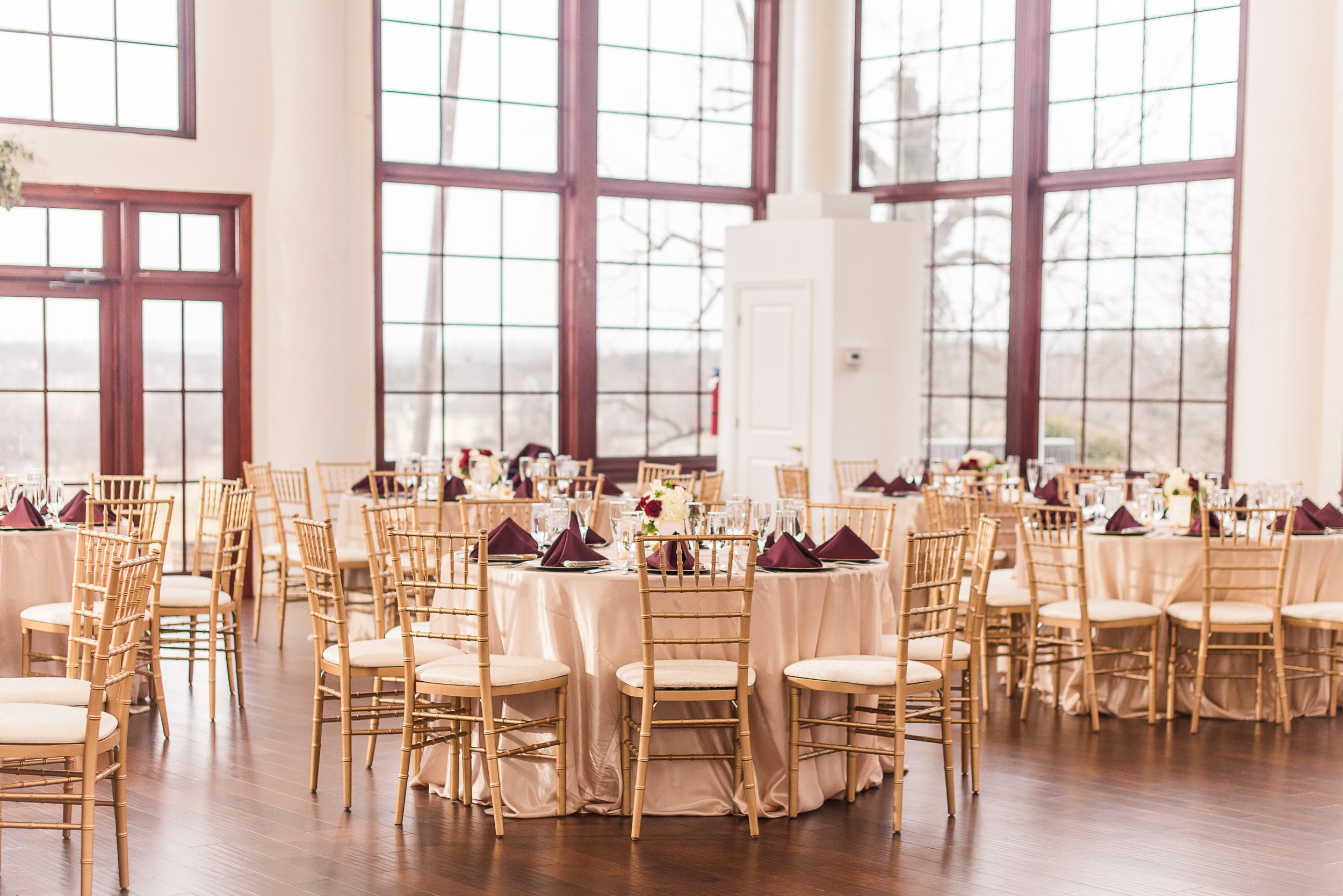 Tables are set with gold chiavari chairs and gold tablecloths inside the ballroom reception space for a wedding at Raspberry Plain Manor in Northern Virginia
