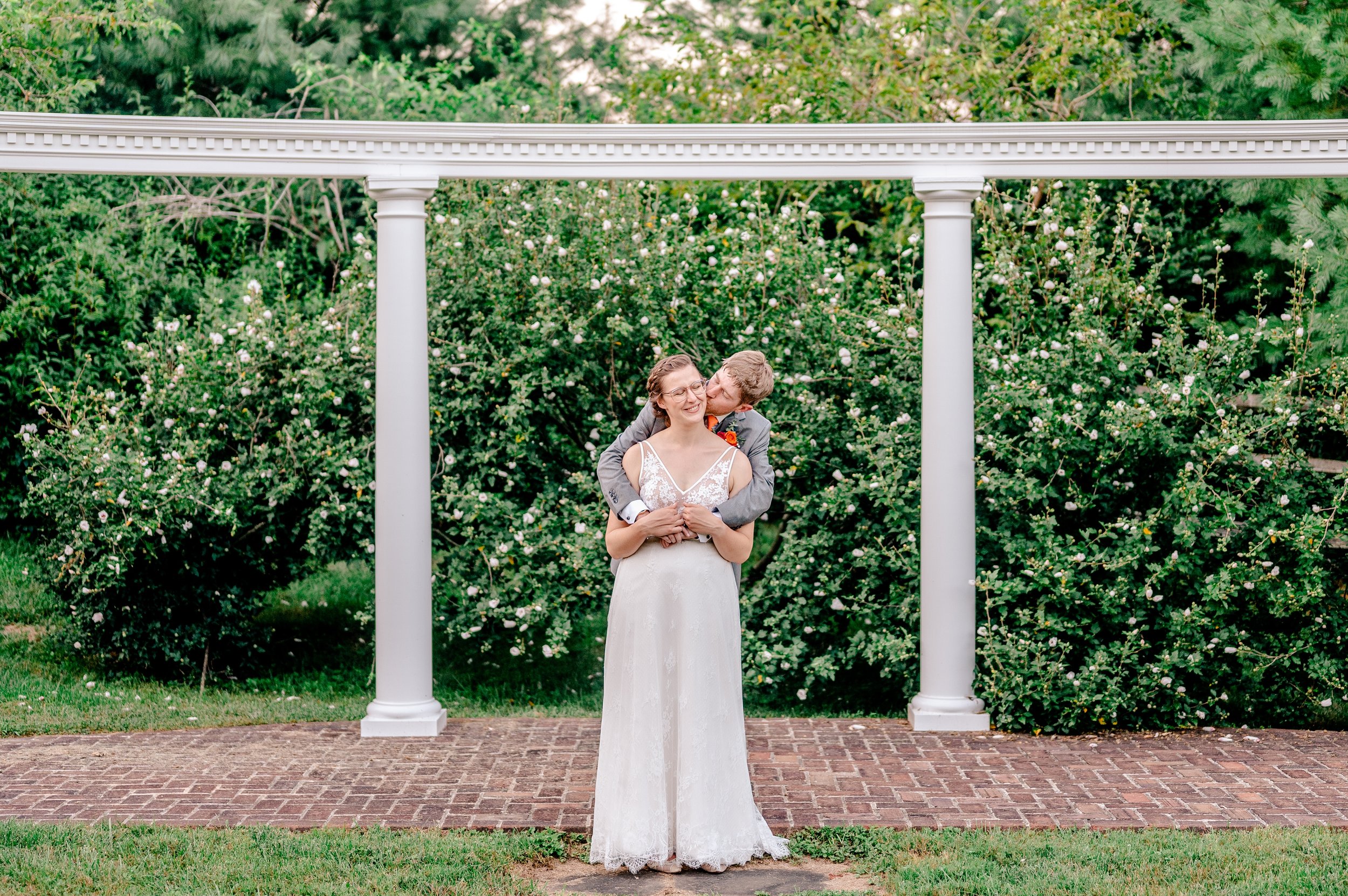 A bride and groom smile in an embrace while standing on the patio during their wedding at Rose Hill Manor in Loudoun County Virginia