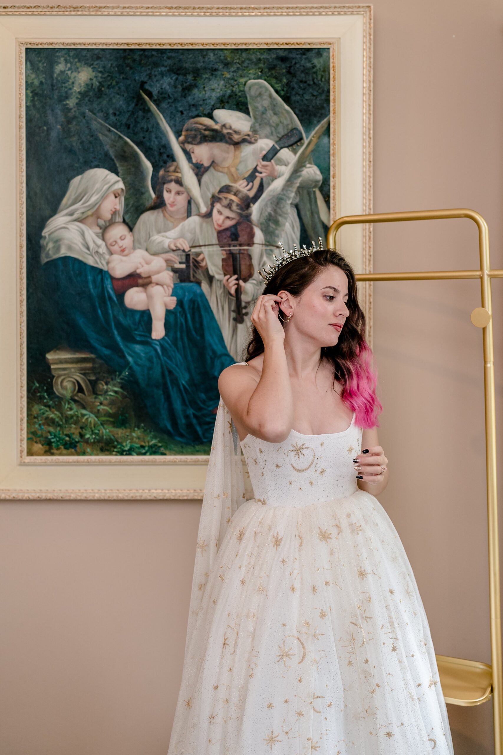A bride wearing a celestial dress adjusts her hair in front of a Renaissance painting before her wedding at Stone Manor Boutique Inn in Loudoun County Virginia
