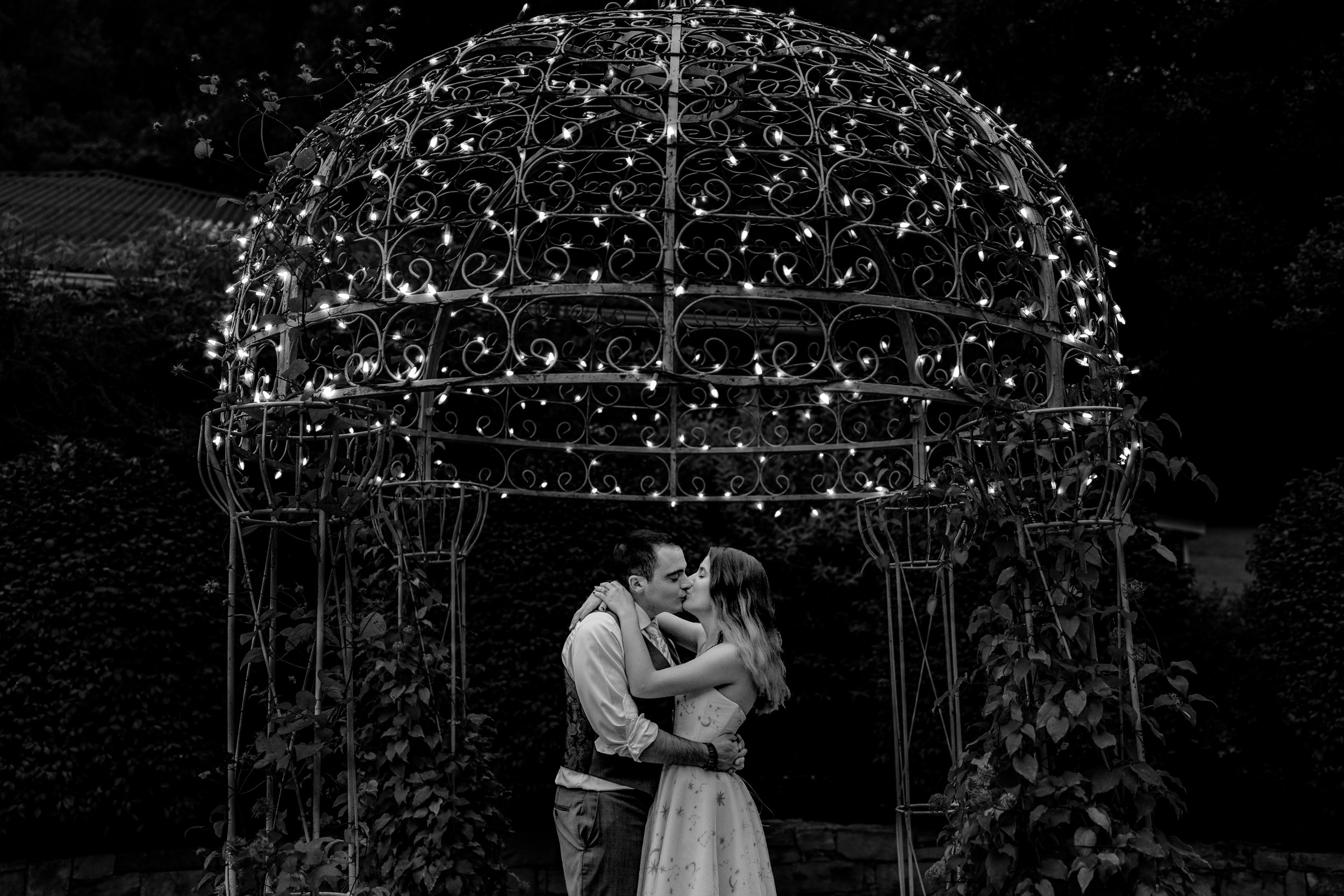 A bride and groom share a kiss under string lights during their wedding at Stone Manor Boutique Inn in Lovettsville, Virginia
