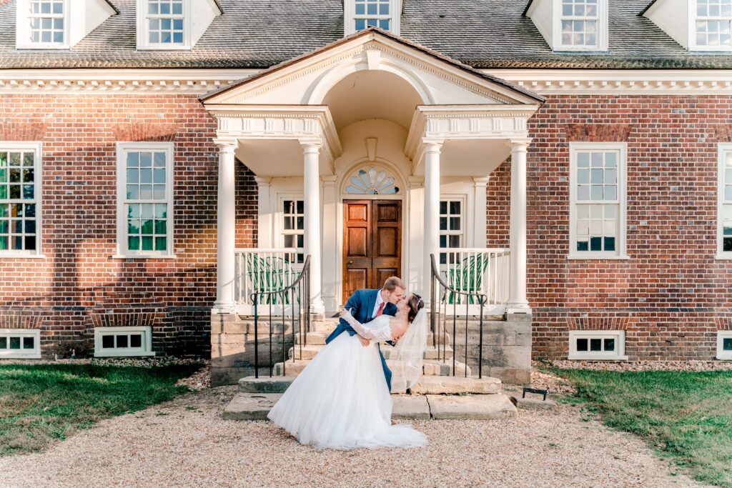 A bride and groom sharing a romantic dip kiss in front of the historic mansion during a wedding at Gunston Hall in Northern Virginia