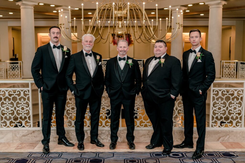 A group of groomsmen posed for an indoor portrait in front of a chandelier