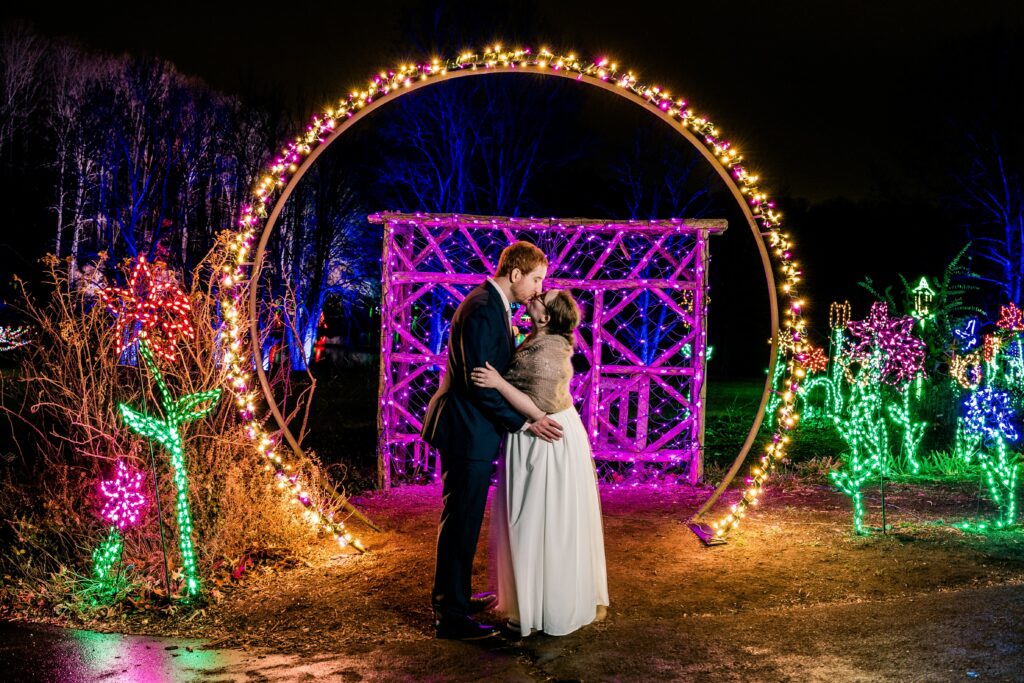A bride and groom share a kiss in front of Christmas lights for a winter wedding at Meadowlark Botanical Gardens in Vienna Virginia