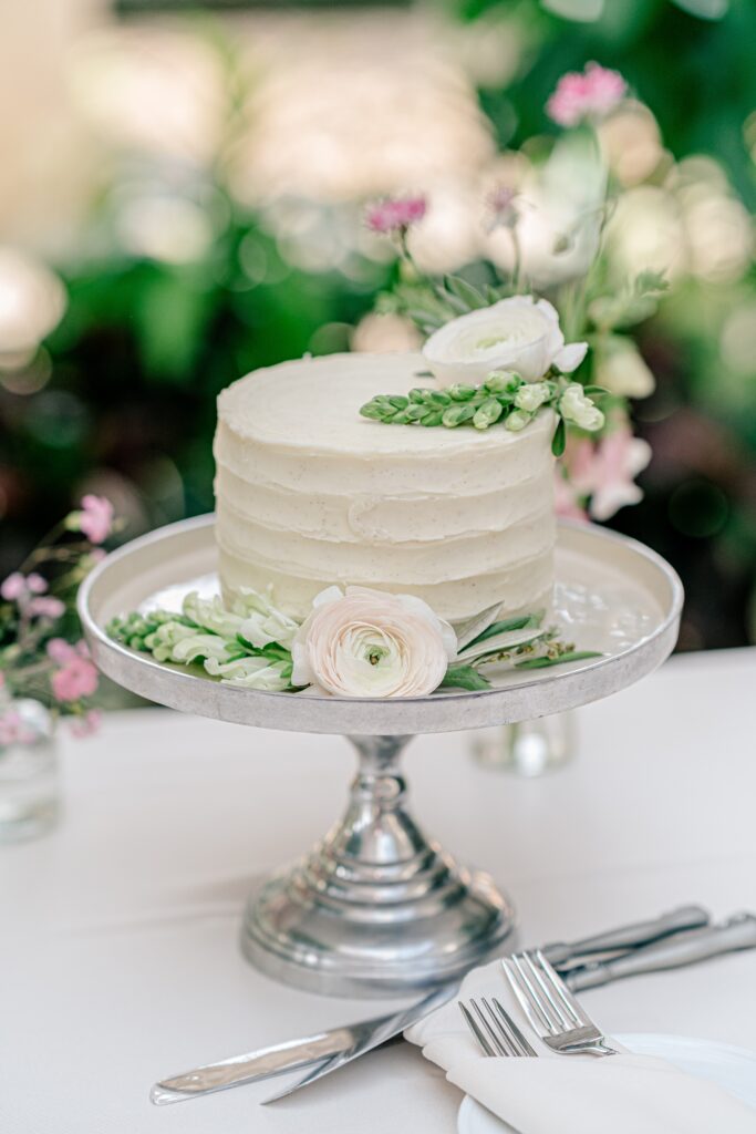 A single tier cutting cake with white frosting decorated with white ranunculus flowers