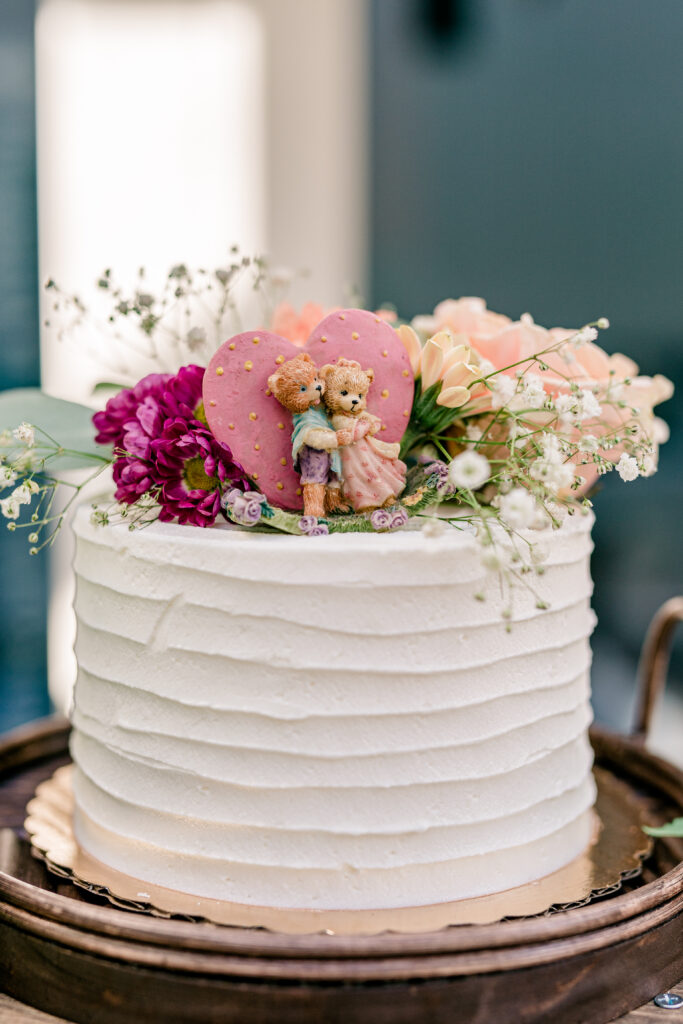 A single tier buttercream cake with a colorful floral topper