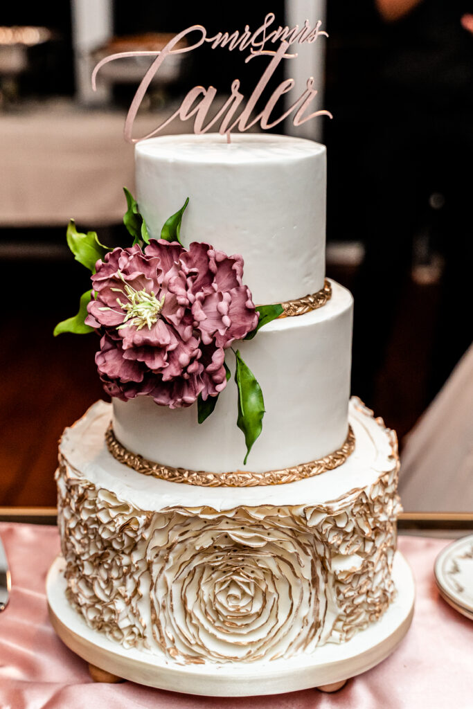 An elegant white and gold wedding cake with a large sugar flower peony