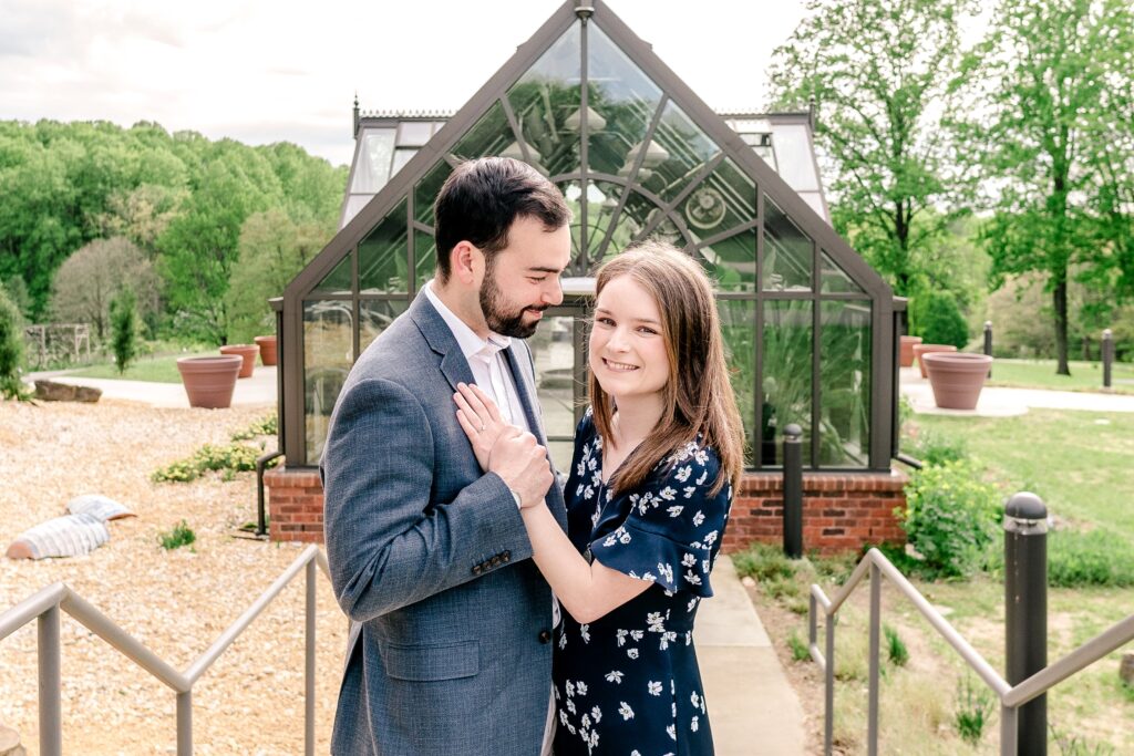 A couple poses together in front of the greenhouse during their Meadowlark Botanical Gardens engagement session