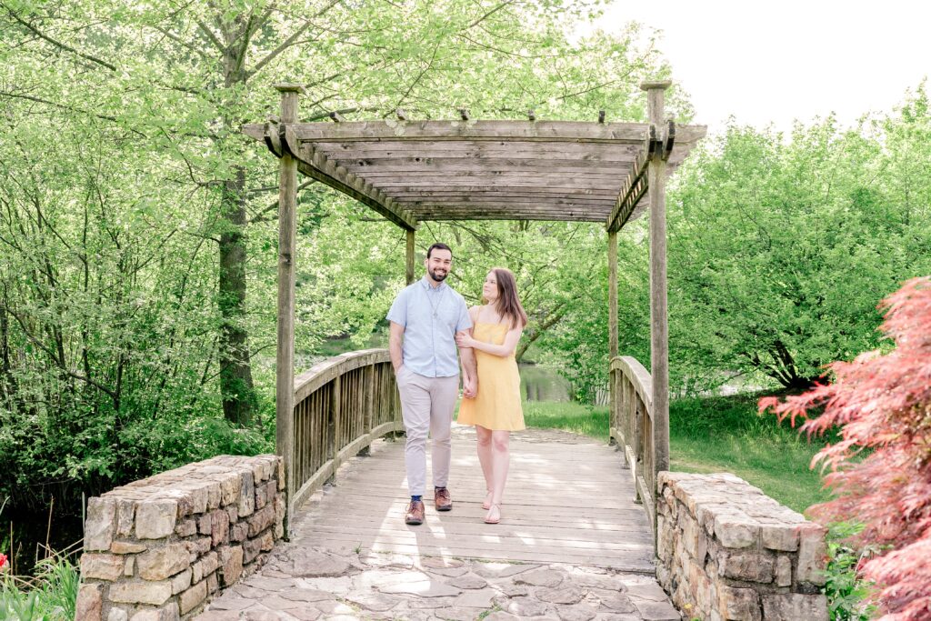 A couple walks together across a wooden bridge during their Meadowlark Botanical Gardens engagement session