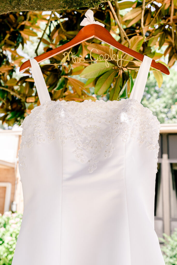 A wedding dress on a personalized hanger hanging from a tree before a wedding at St Philip Catholic Church in Falls Church Virginia