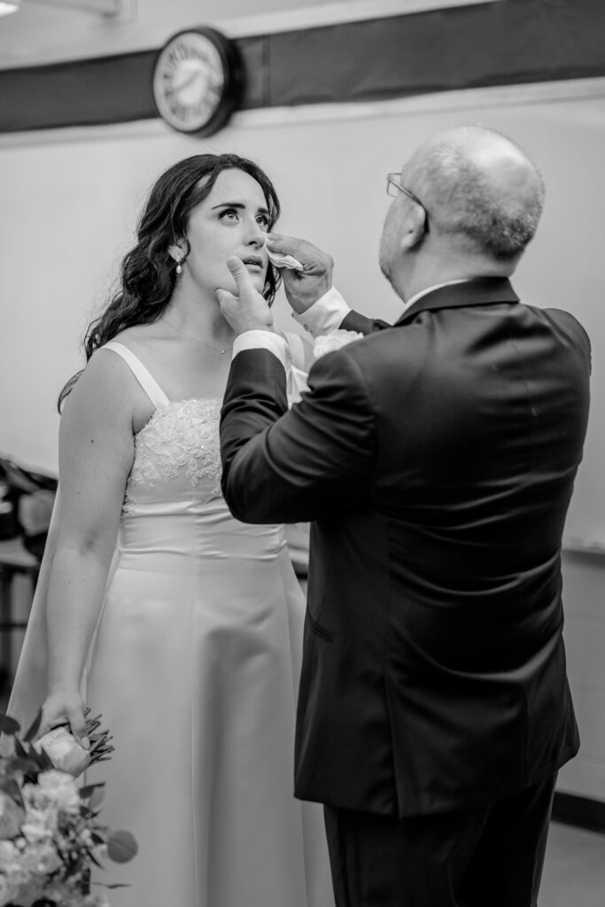 A father wiping tears from his daughter's face as she prepares for her wedding at St Philip Catholic Church in Falls Church Virginia