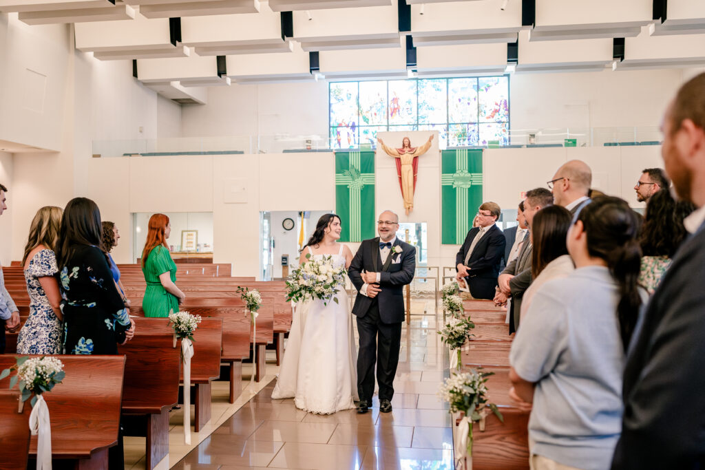 A bride and her father walking down the aisle during a wedding at St Philip Catholic Church in Falls Church Virginia