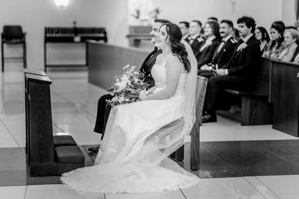 A bride and groom laughing during the homily of a wedding at St Philip Catholic Church in Falls Church Virginia