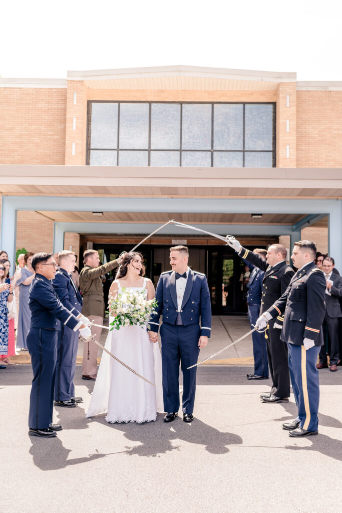 A bride and groom smiling during their saber arch exit after a wedding at St Philip Catholic Church in Falls Church Virginia