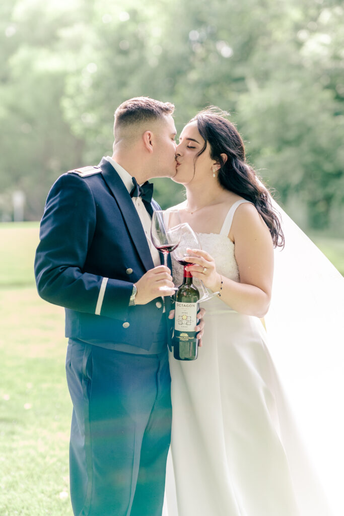 A bride and groom share a kiss while toasting with a special glass of wine during a tented wedding reception at Historic Blenheim in Fairfax, Virginia