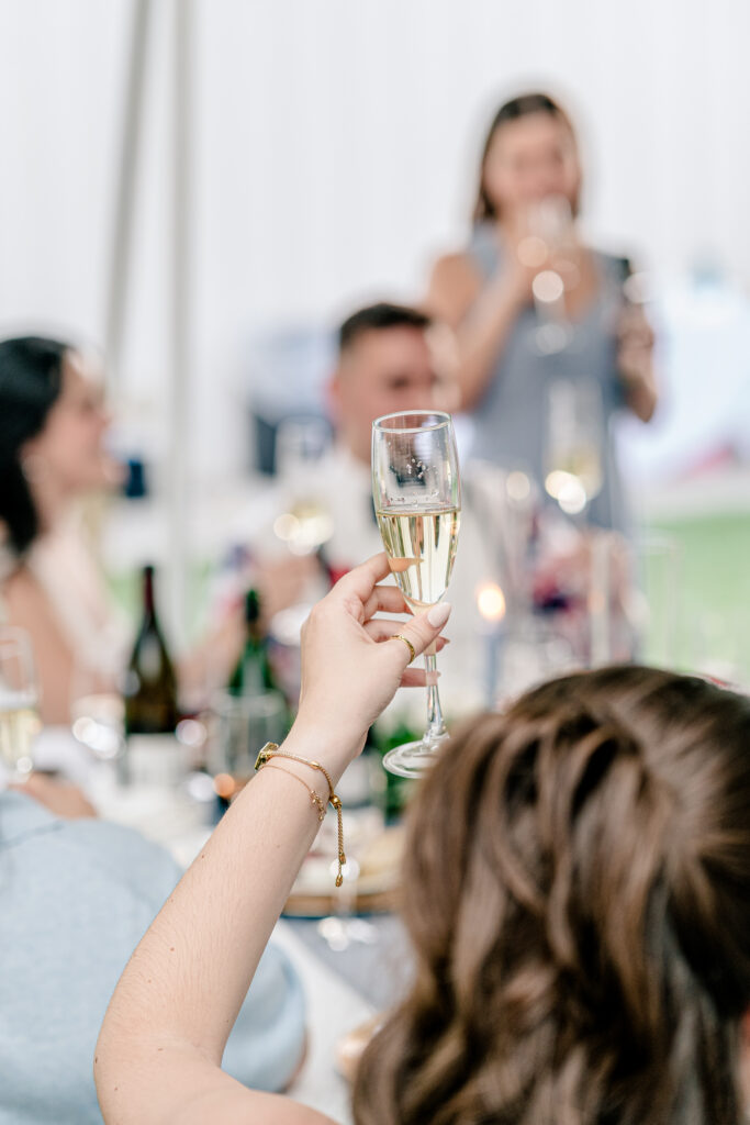 A guest raising her champagne glass for a toast during a tented wedding reception at Historic Blenheim in Fairfax, Virginia