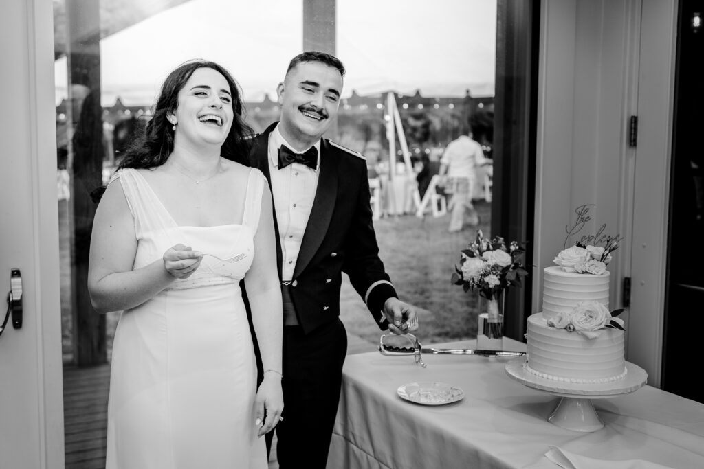 A bride and groom laughing together after their cake cutting during a tented wedding reception at Historic Blenheim in Fairfax, Virginia