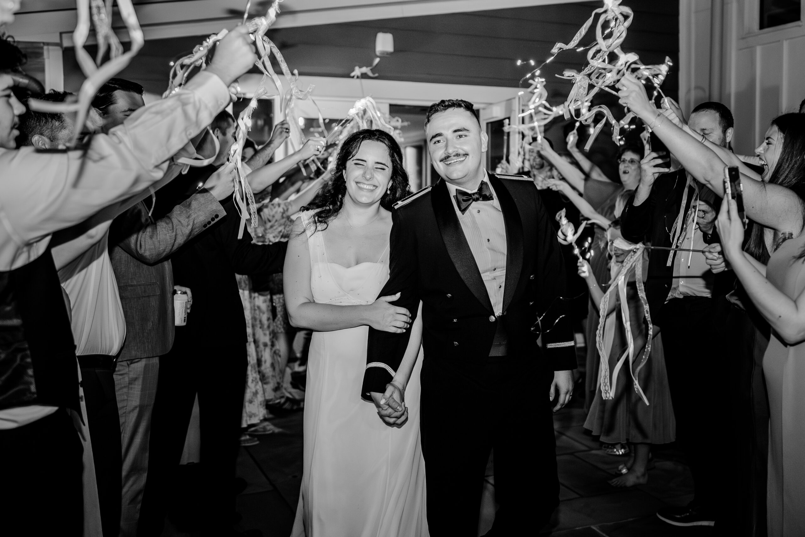 A bride and groom smile as they go through a tunnel between wedding guests waving light up ribbons after their tented wedding reception at Historic Blenheim in Fairfax Virginia