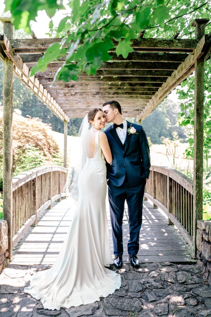 A groom kisses his bride on the cheek as she turns over her shoulder during a micro wedding at Meadowlark Botanical Gardens in Vienna, Virginia