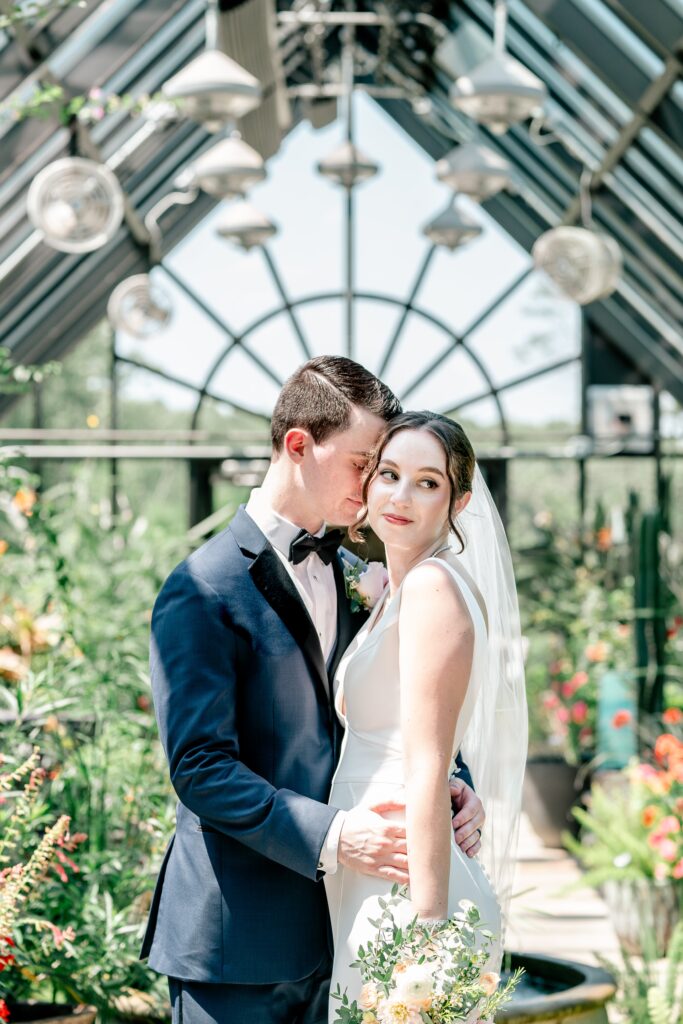 A bride looks over her shoulder as her groom nuzzles into her during a micro wedding at Meadowlark Botanical Gardens in Vienna, Virginia