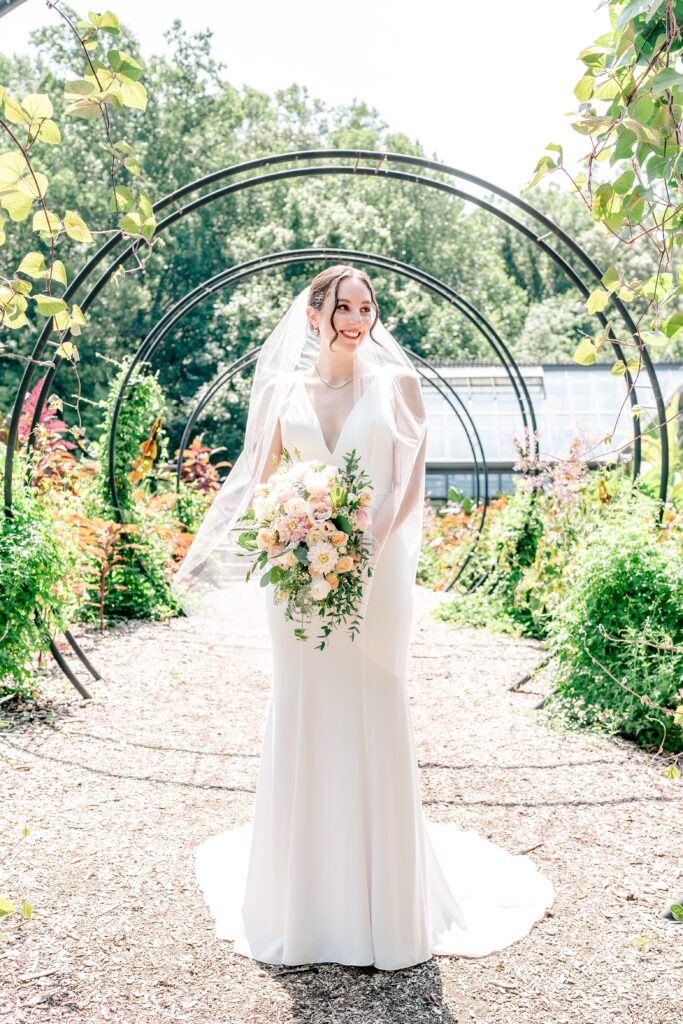 A bride smiles at her groom off camera while posing for a classic portrait during a micro wedding at Meadowlark Botanical Gardens in Vienna, Virginia