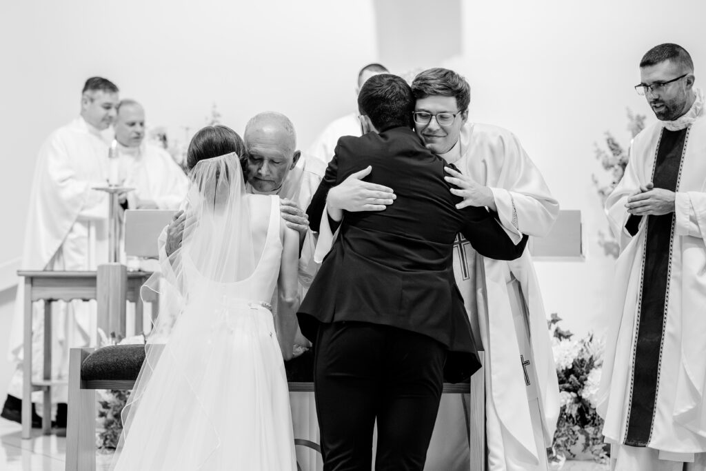 Priests hug the newlyweds during a wedding at St. Joseph Catholic Church in Herndon, Virginia