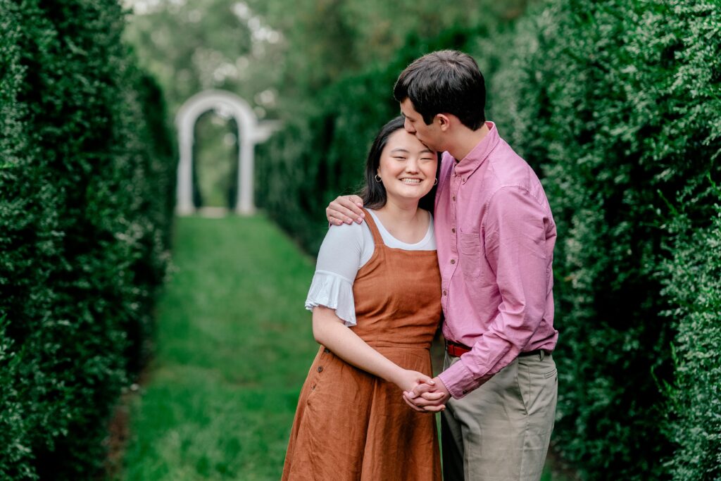 A man kisses the forehead of his fiancée as they hold hands.