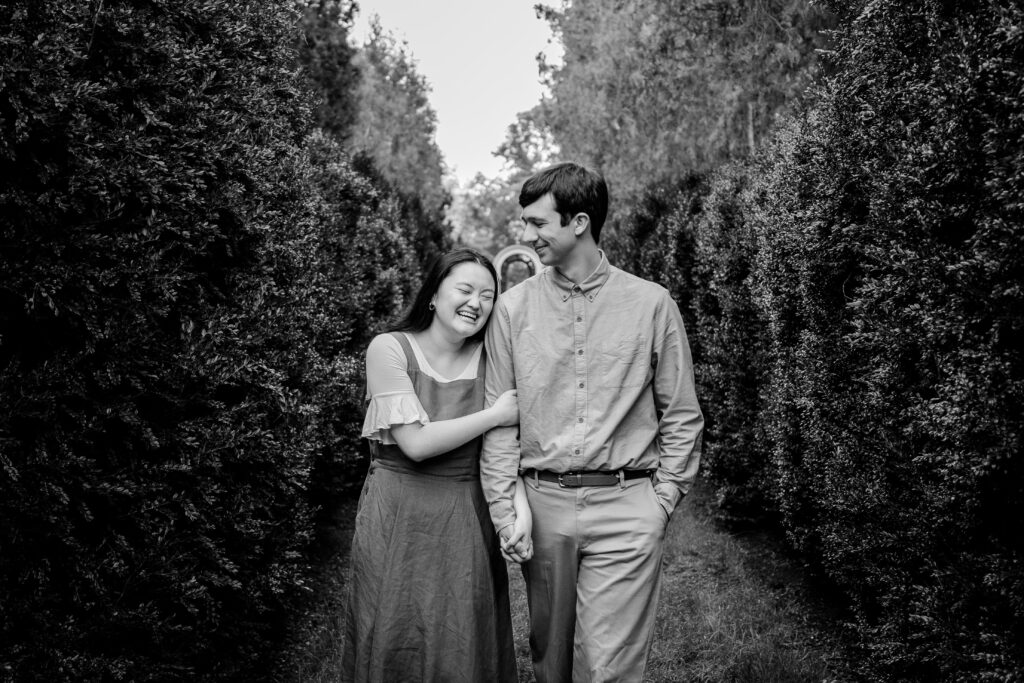 An engaged couple holds hands and laugh as they walk together through a secret garden