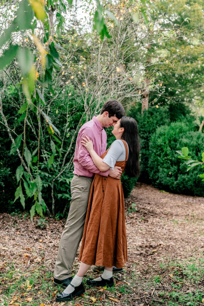 An engaged couple share an intimate moment forehead to forehead surrounded by greenery