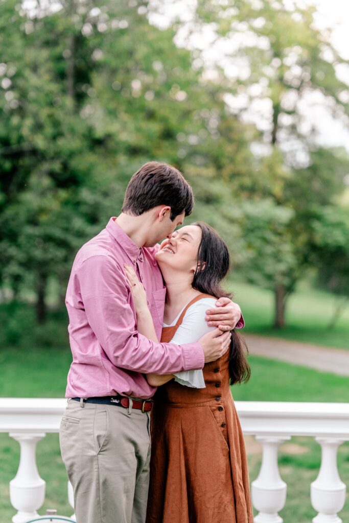 A woman closes her eyes and smiles up at her fiancé in front of a decorative fence