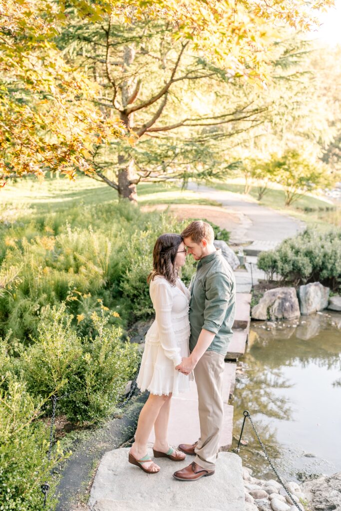 A couple standing together on a bridge holding hands during their Brookside Gardens engagement session in Silver Spring, MD