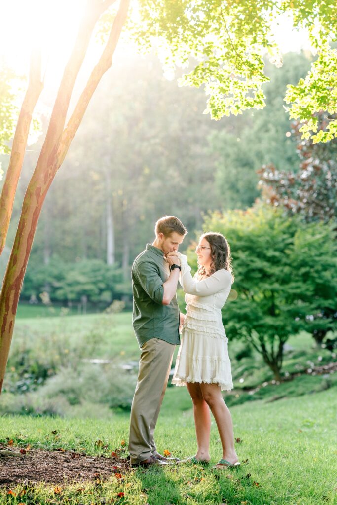 A man kissing his fiancée’s hand during their Brookside Gardens engagement session in Silver Spring, MD