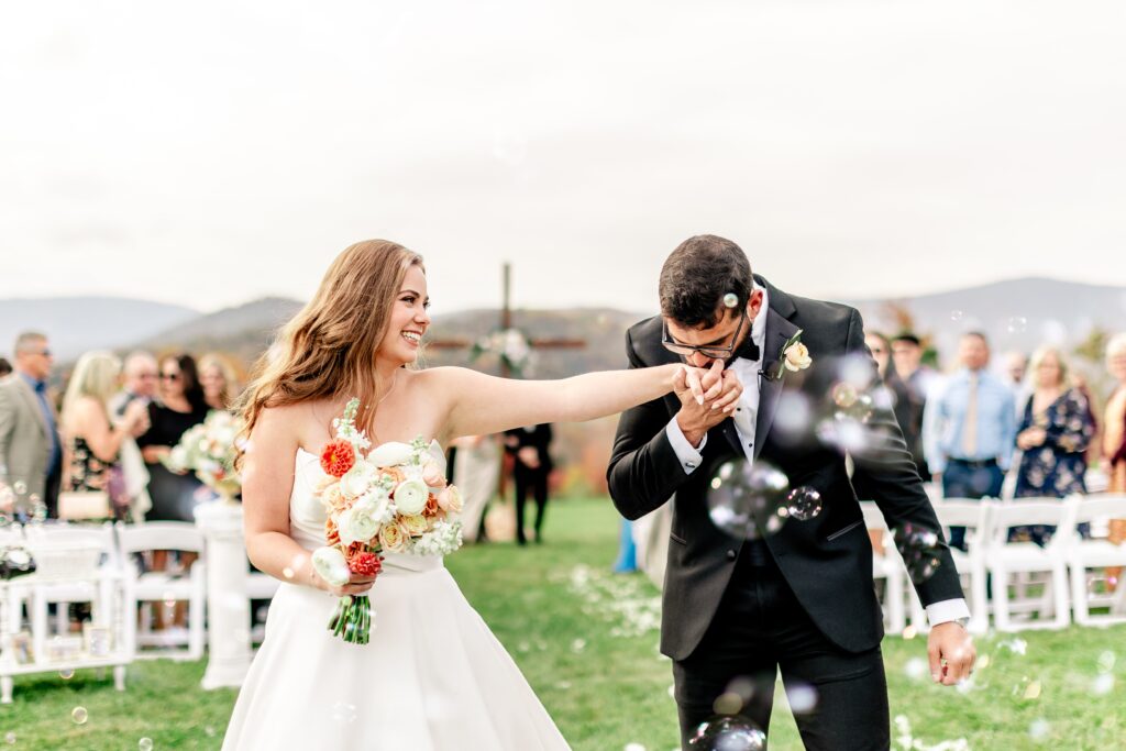 A groom kisses the hand of his bride during a bubble sendoff for a wedding at The Barn at Edgewood