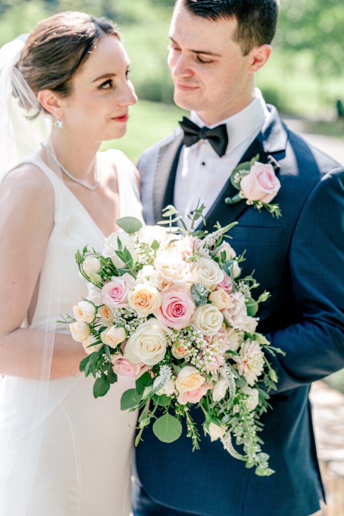 A bride and groom looking at each other as the camera focuses on a vibrant bouquet during a wedding at The Atrium at Meadowlark Botanical Gardens