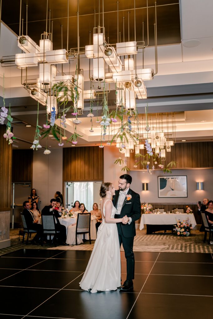 A bride and groom share their first dance in a hotel ballroom with a gorgeous floral installation by Floriography VA