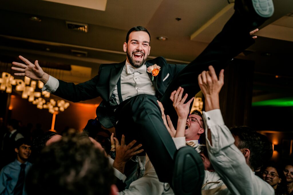 A groom smiling as his groomsmen throw him in the air on the dance floor of his ballroom wedding reception in Northern Virginia