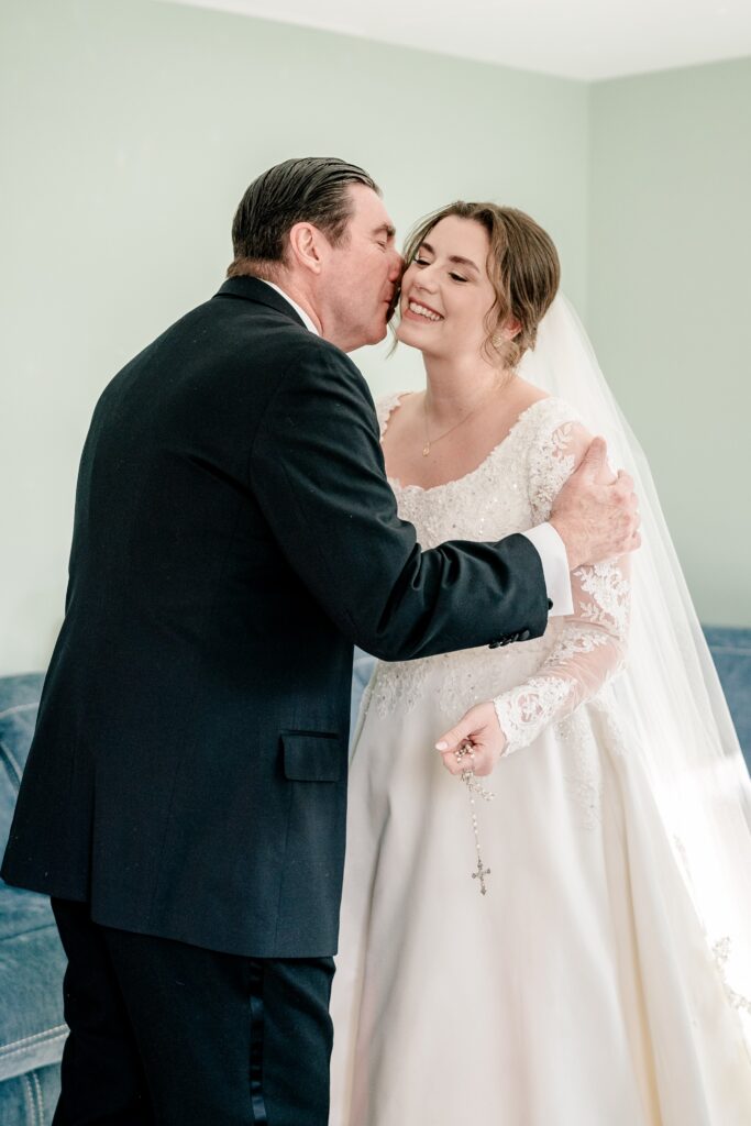 A father kisses his daughter on the cheek during her Catholic wedding in Northern Virginia