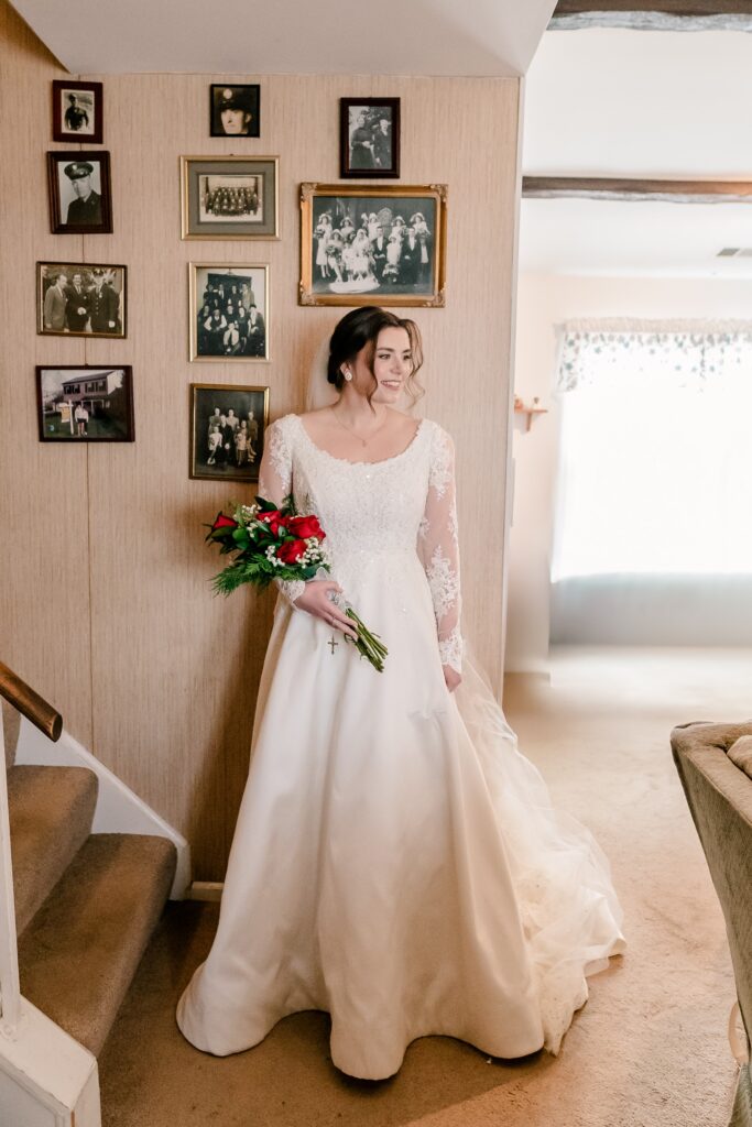 A bride stands beside a gallery wall of family photos before her Christmas themed wedding