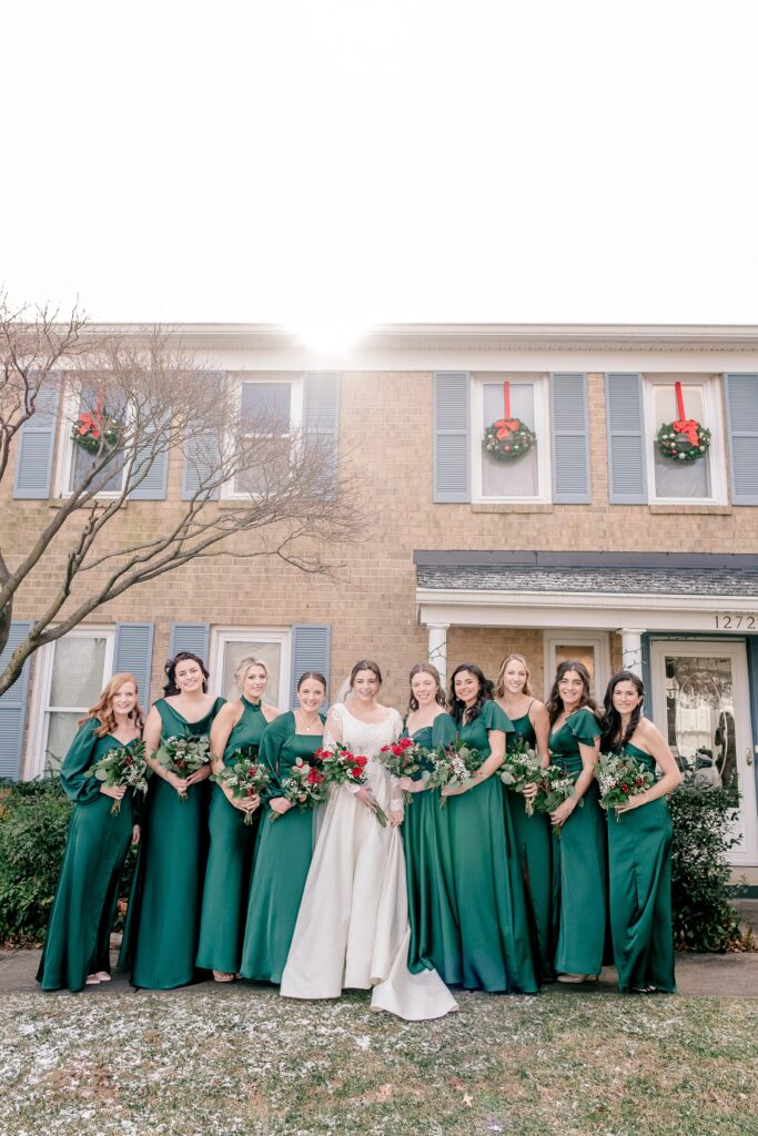 A bride and her bridesmaids in green pose for a photo outside her house before her Christmas themed wedding