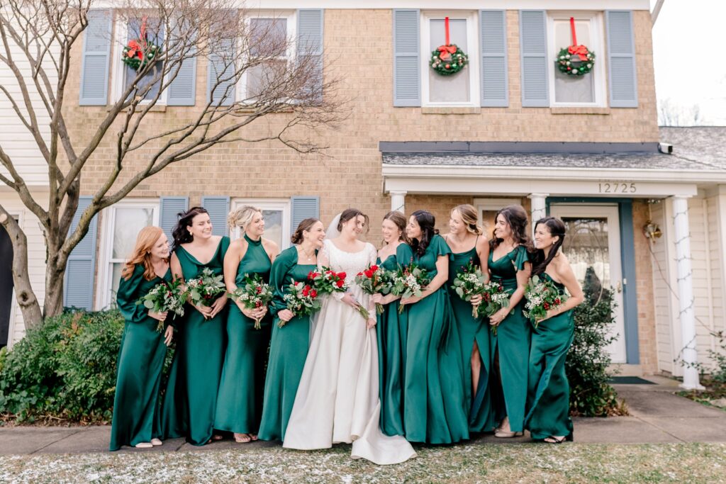 A bride smiles at her bridesmaids as they pose outside her house before her Catholic wedding