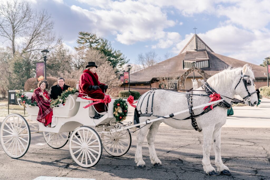 The parents of the bride smile at the camera from inside a horse drawn carriage for a Catholic wedding in Northern Virginia