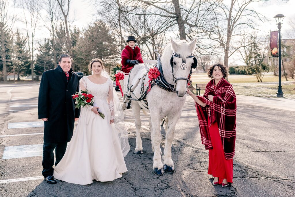 A bride and her parents pose beside a horse drawn carriage for a Christmas themed wedding