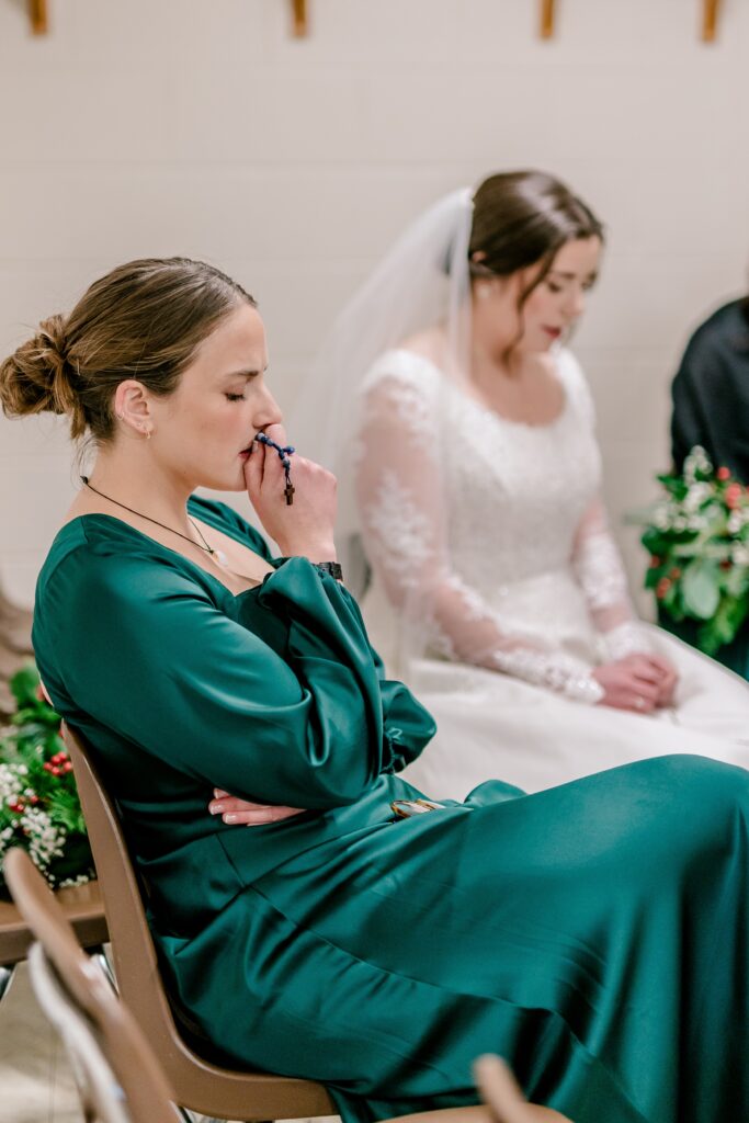 A bridesmaid holds her rosary to her face as she prays with the bridal party before a Catholic wedding