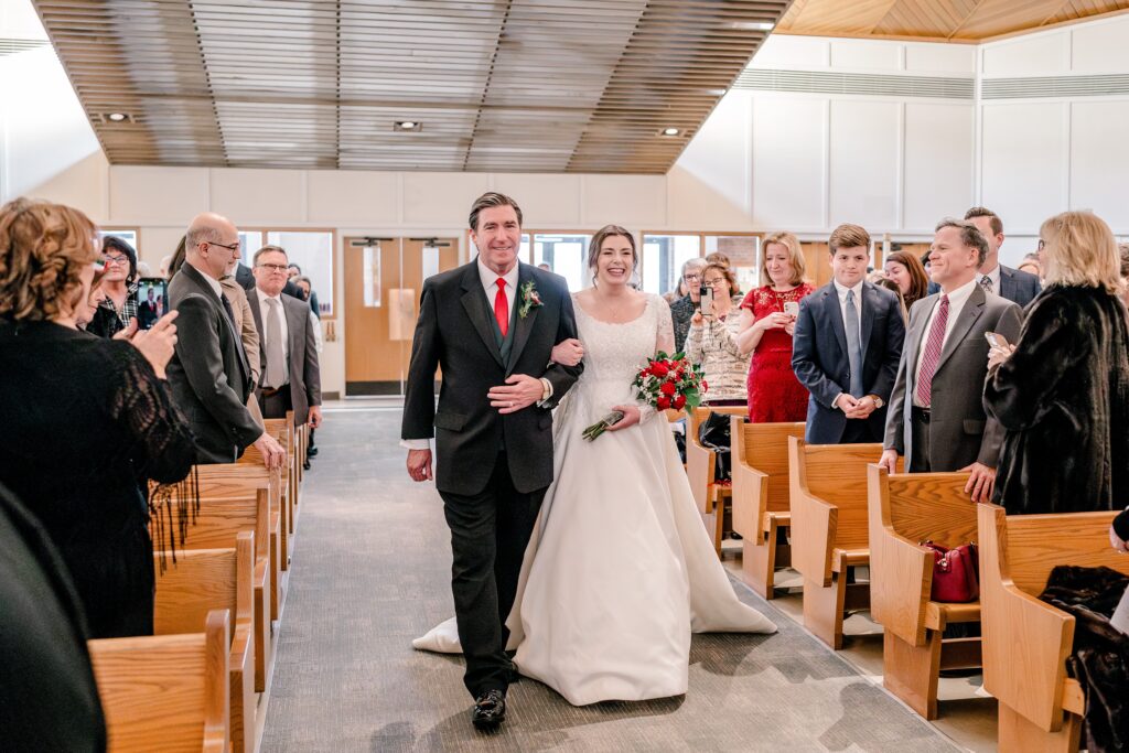 A bride and her father walking down the aisle during a Christmas themed wedding at St. Joseph Catholic Church in Herndon Virginia