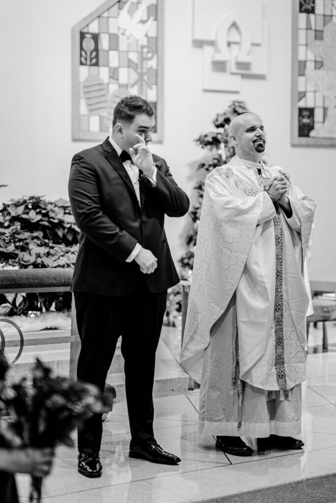 A groom wiping away a tear as he sees his bride for the first time during their Catholic wedding