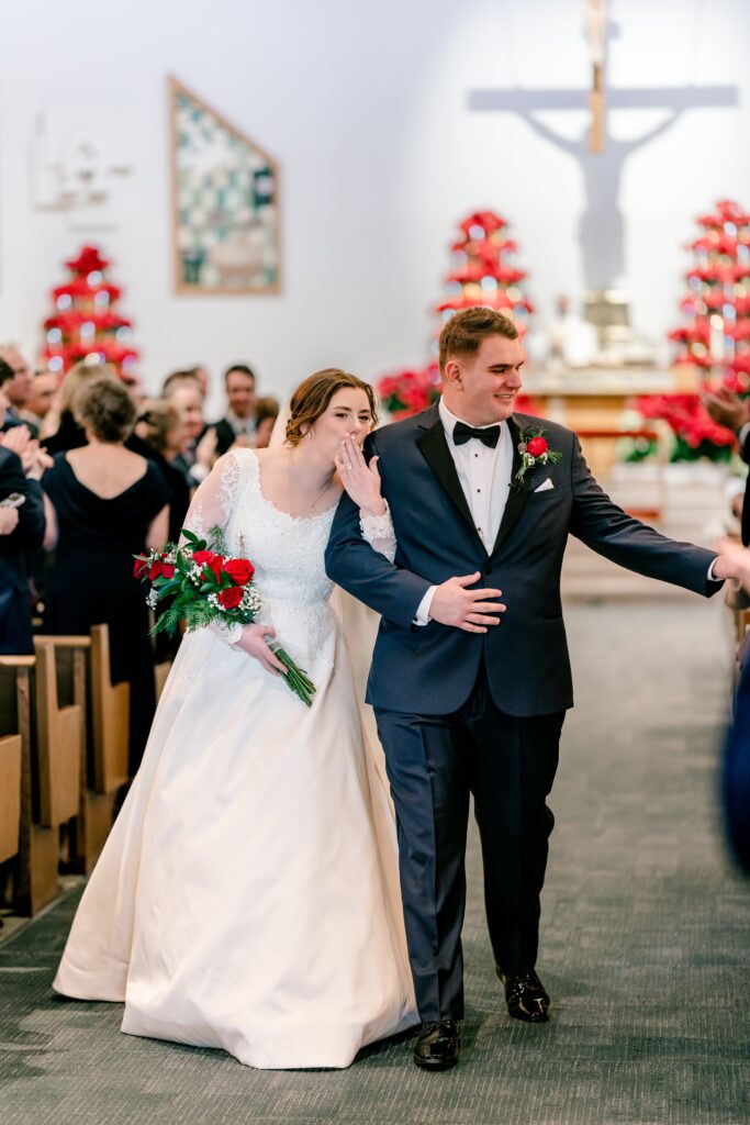 A groom shakes hands as the bride blows a kiss exiting their Catholic wedding in Northern virginia